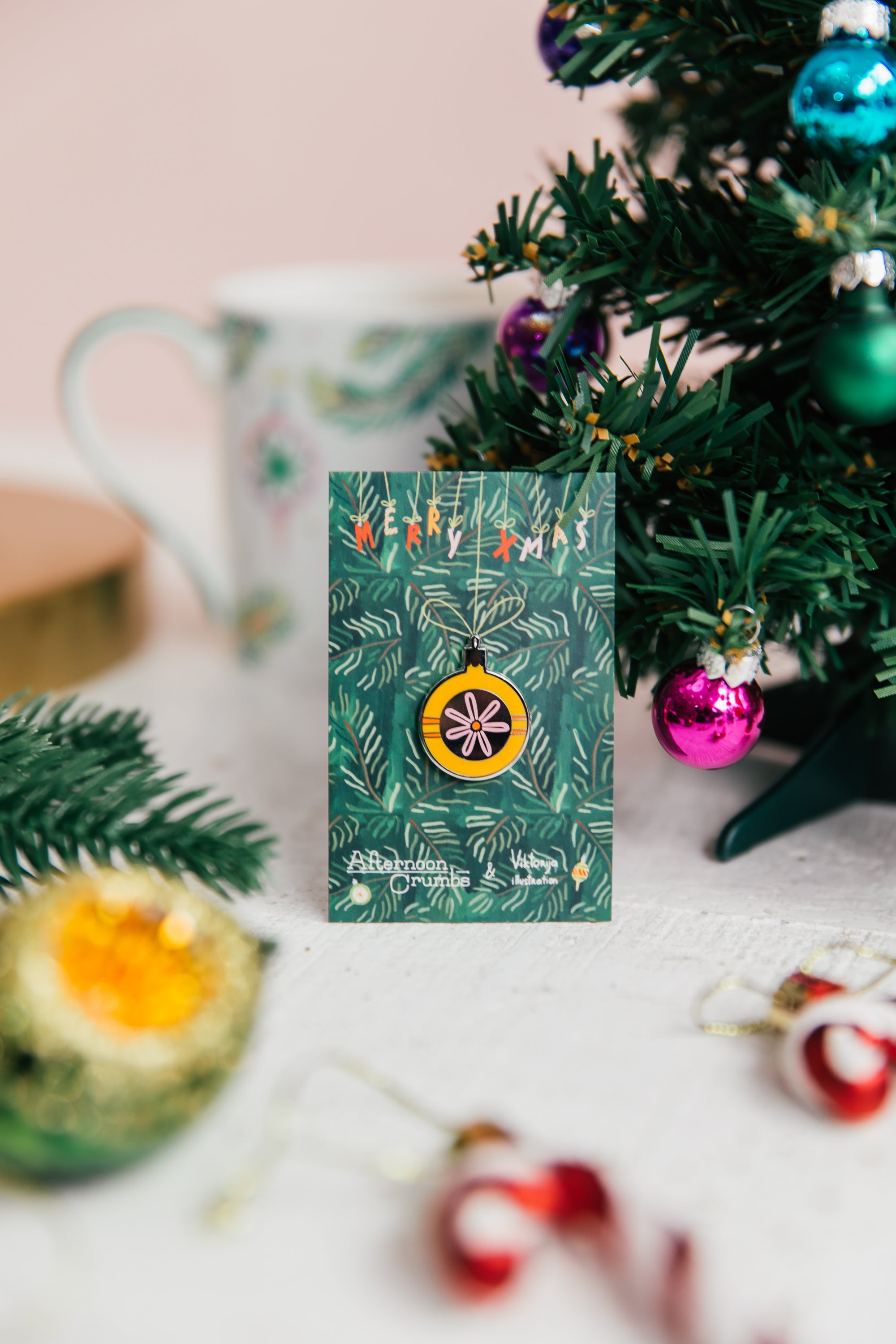 Enamel Bauble Pin on Backer next to Christmas Tree