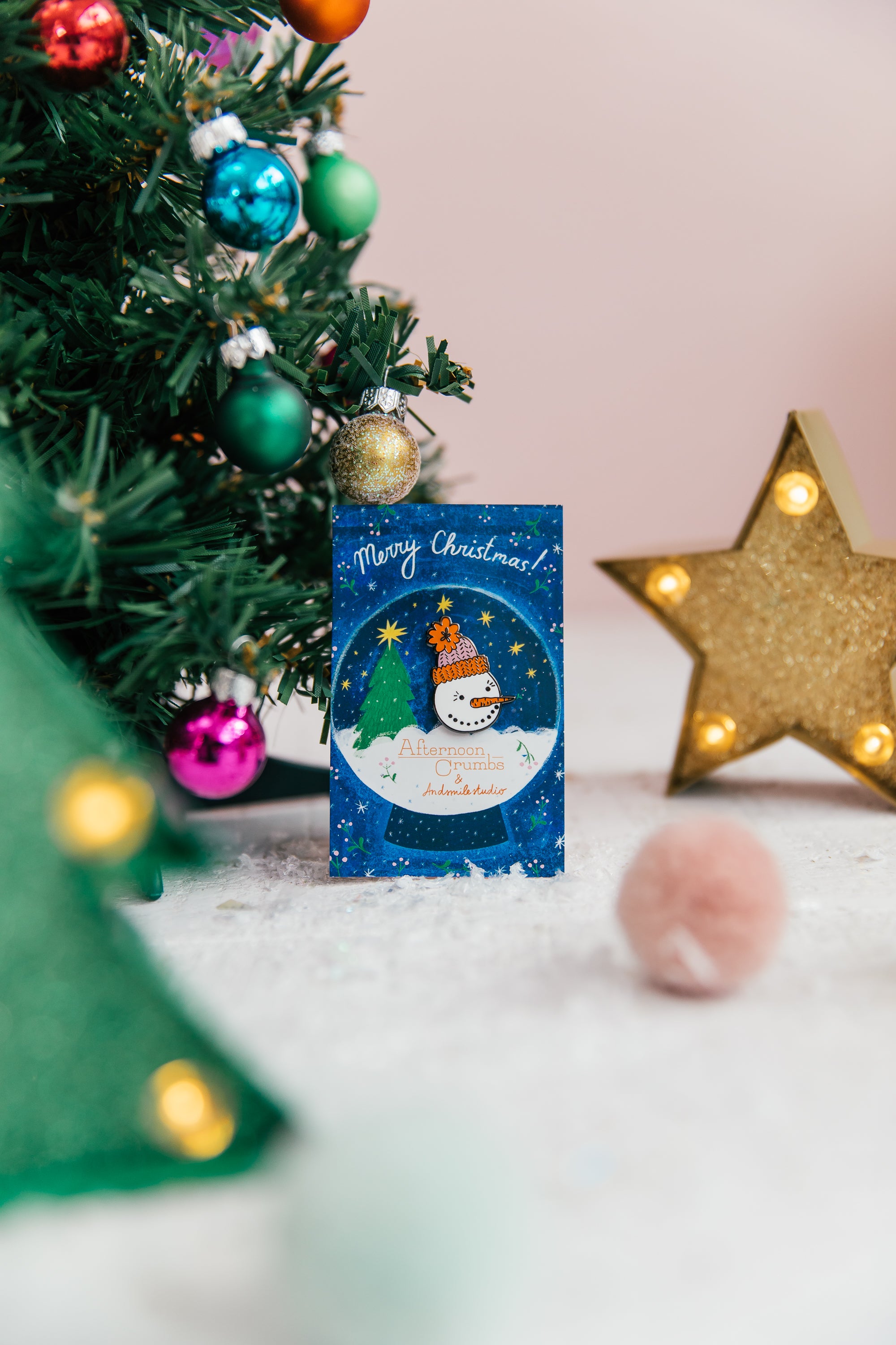 Snowman Enamel Pin on Backer next to Christmas Tree