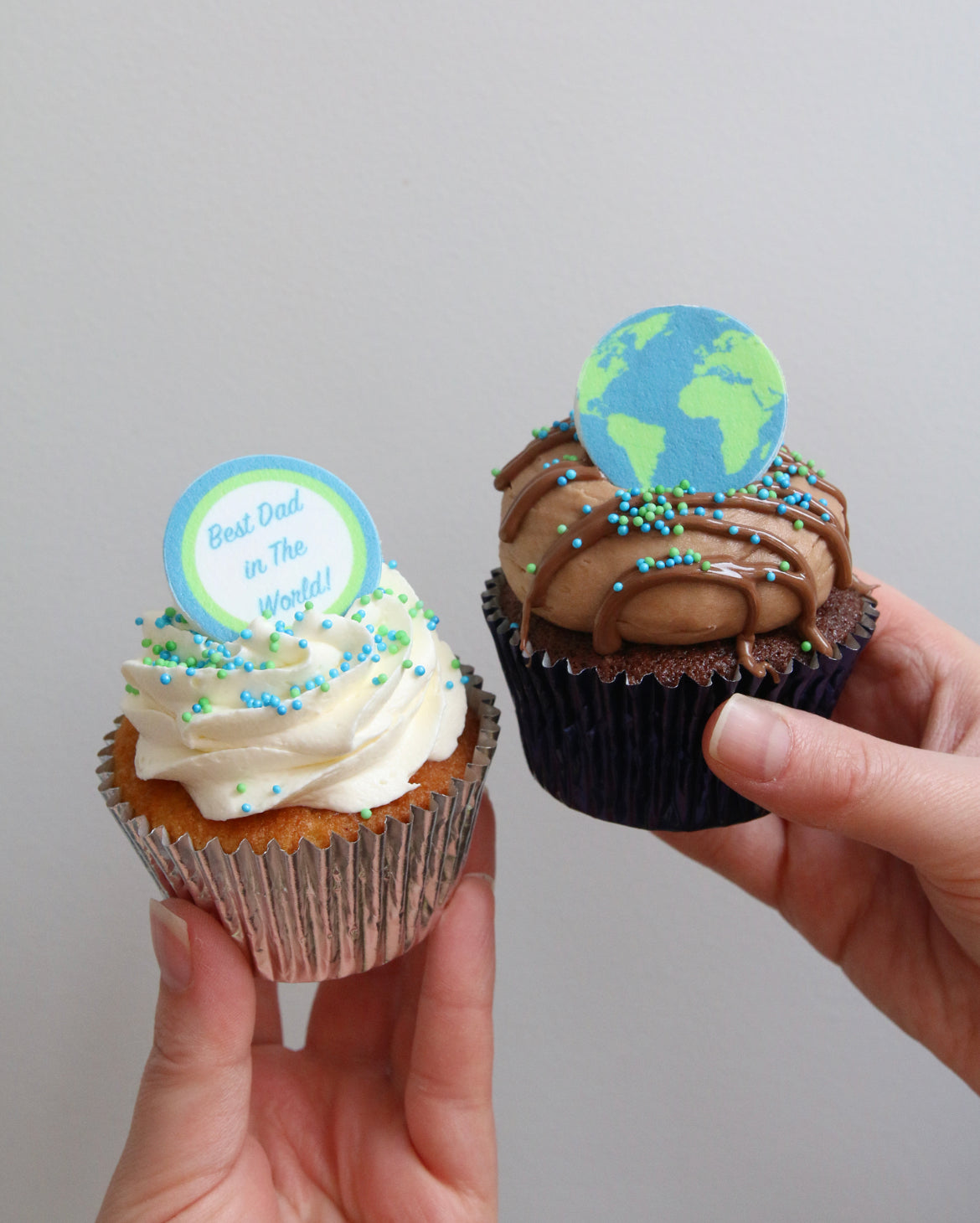 Holding Two "Best Dad in The World" Cupcakes