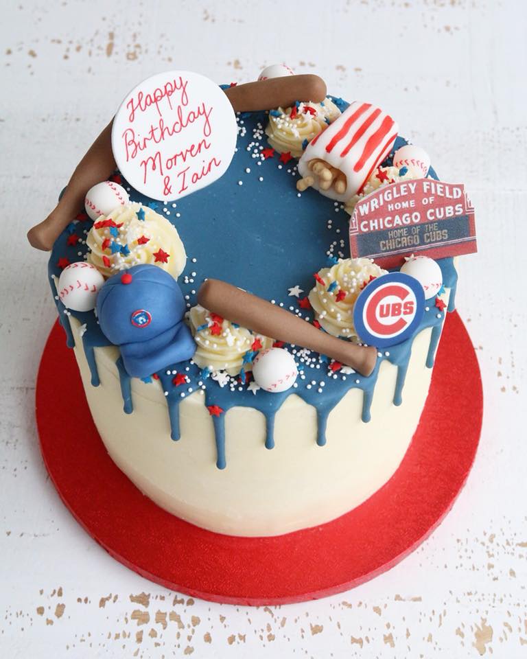 Birthday drip cake with Chicago Cubs theme including baseball bat, ball, and Wrigley Field stadium sign.
