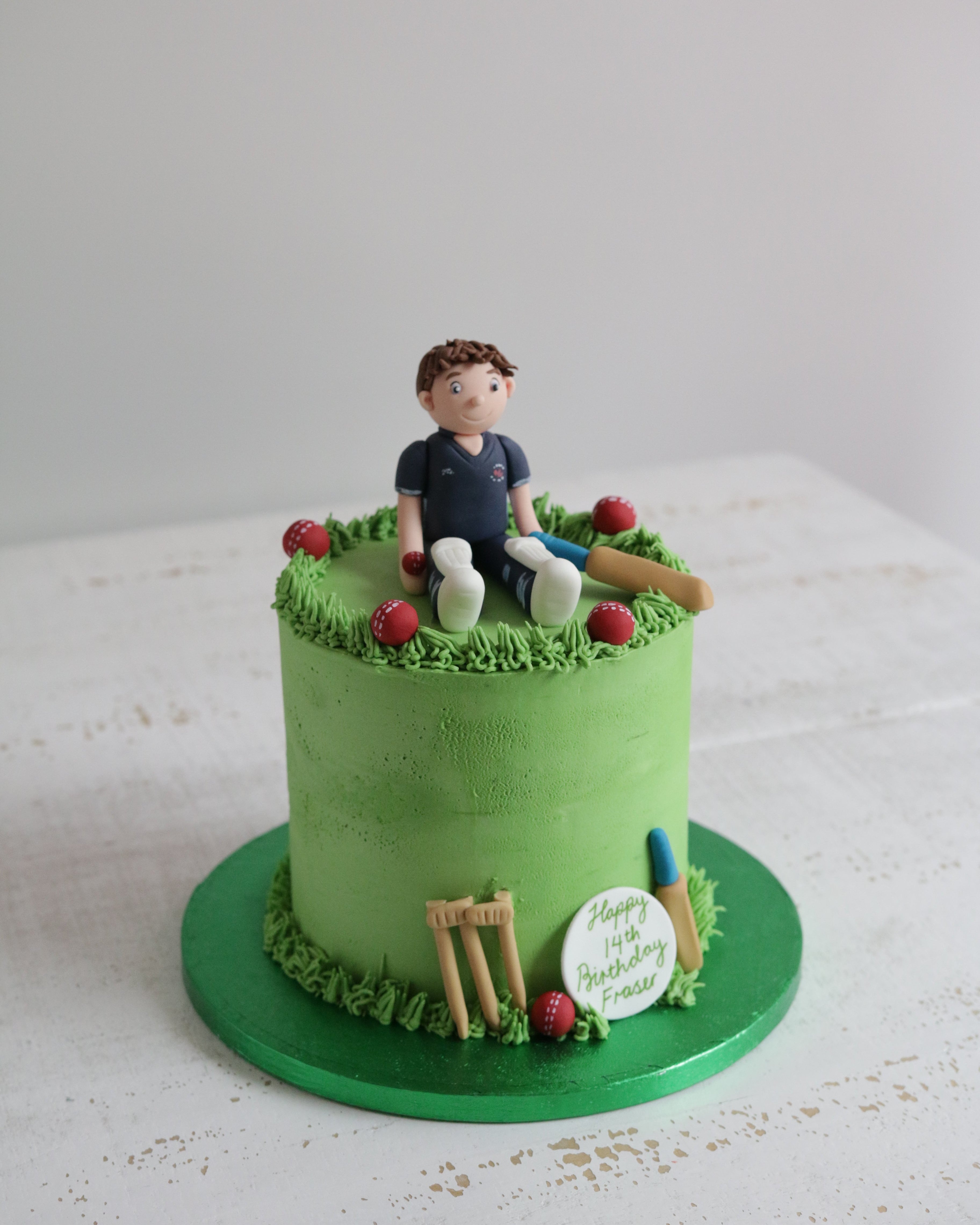 Green cake with a cricket-themed decoration including a figure of a player, wickets, and a ball.