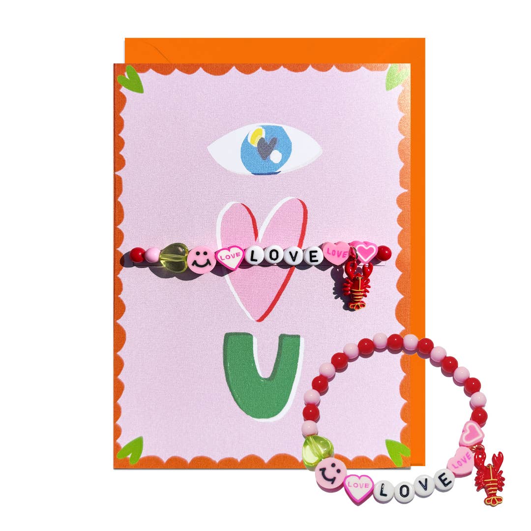 An Eye Love U greeting card with bracelet with pink, red, and green beads, smiley face charms, and letter beads spelling LOVE, displayed on a pink and orange decorative card