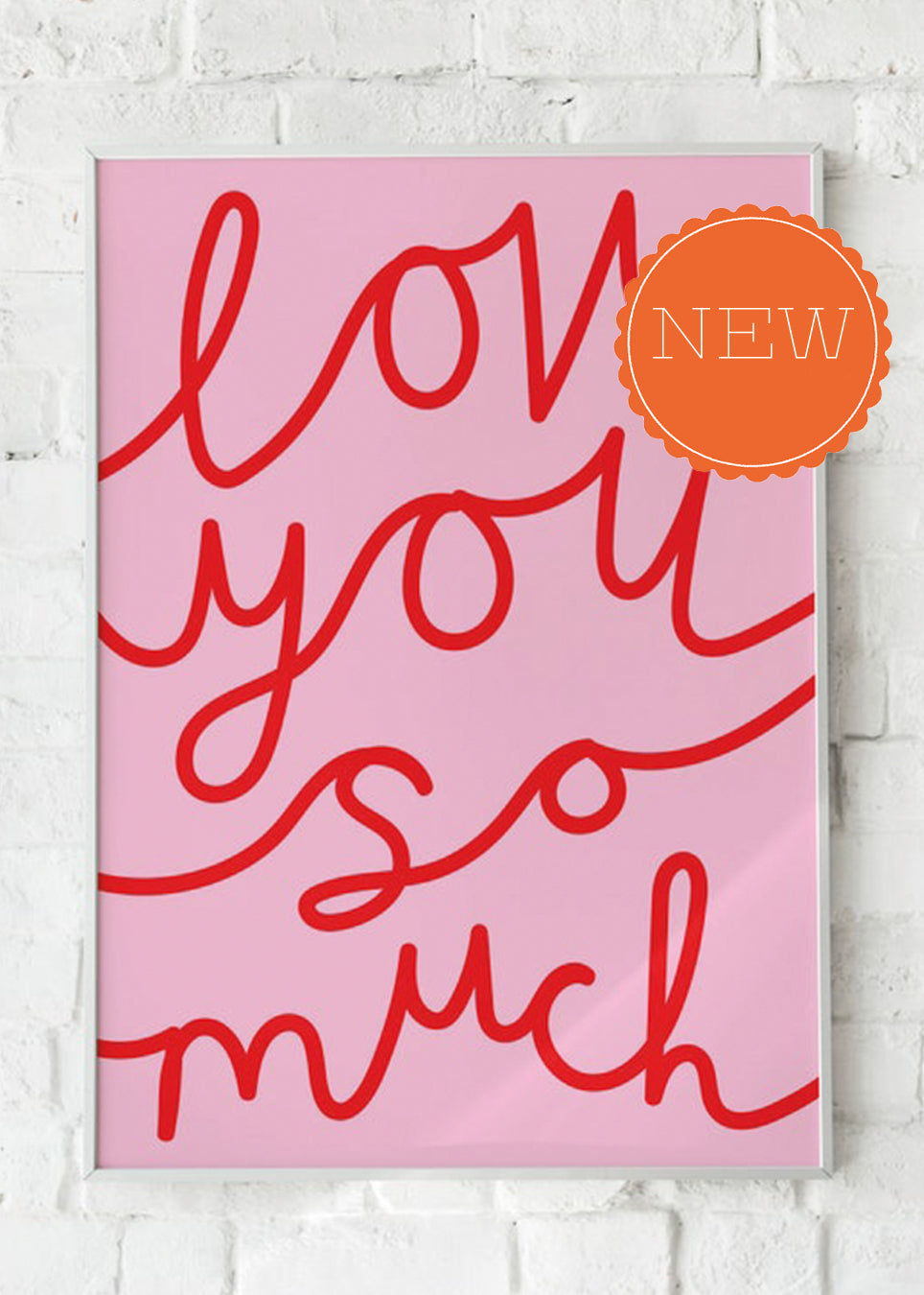 A framed typographic wall art print with the phrase "love you so much" in red script on a pink background, hung against a white brick wall. An orange circular "NEW" badge is overlaid in the top right.