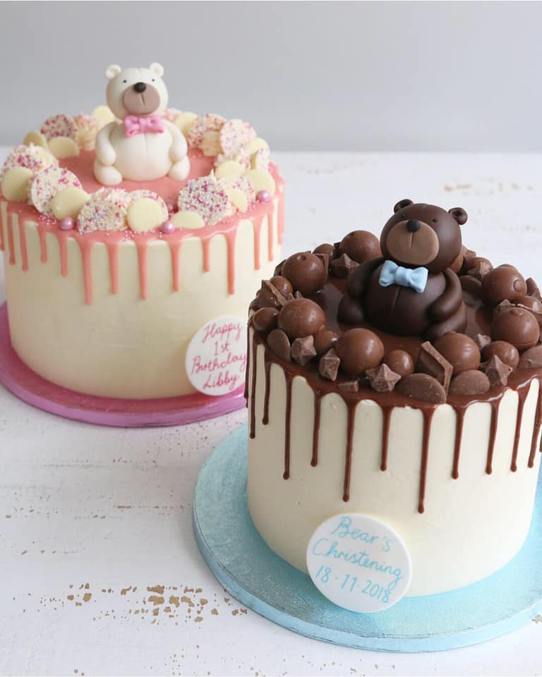 Two Drip Cakes - one with pink drip decorated with white chocolates and a white teddy with pink bow, the other with a milk chocolate drip decorated with milk chocolates and a brown teddy with a blue bow 