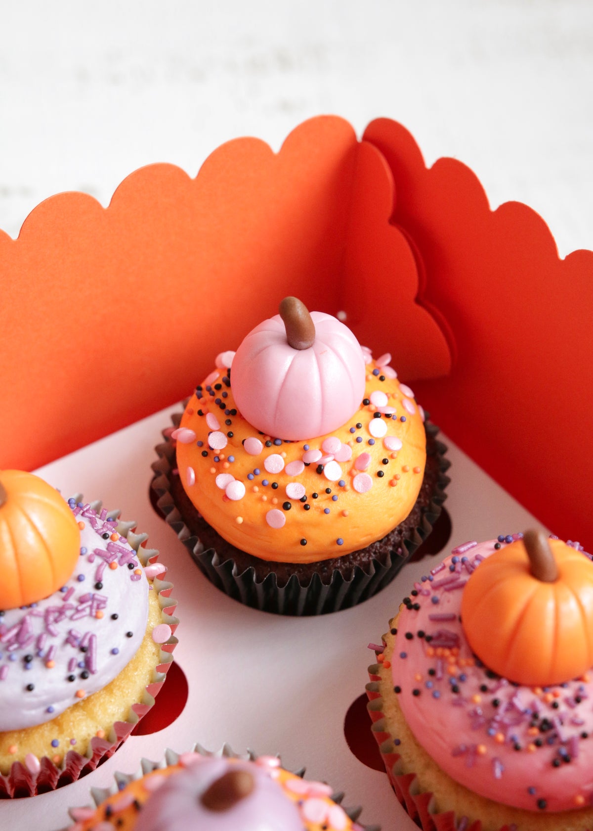 Close up on a Halloween cupcake in a box topped with orange vanilla buttercream and a pink fondant cupcake