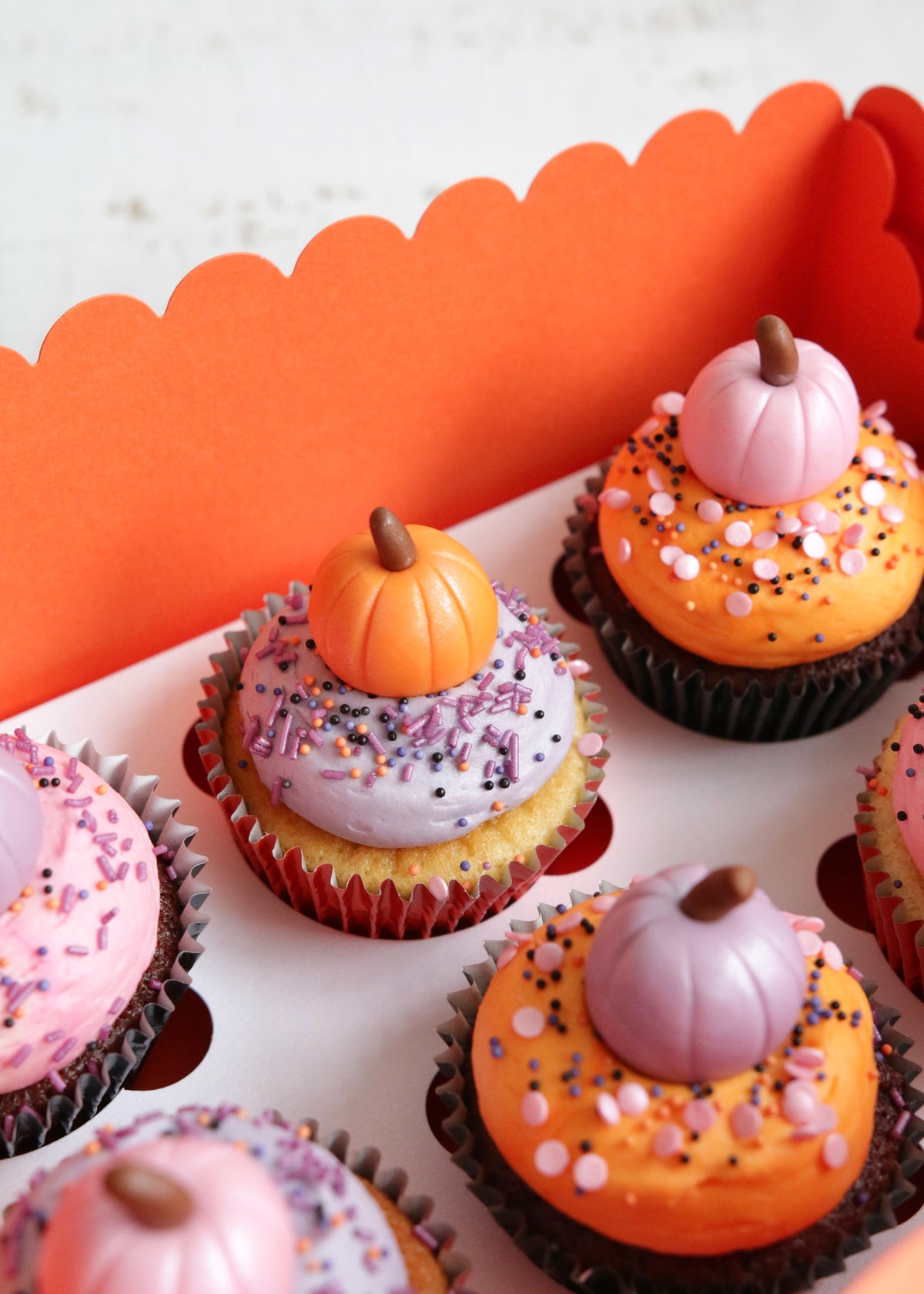 Close up on a box of Halloween cupcakes topped with pastel pink, orange and purple buttercream and fondant pumpkins