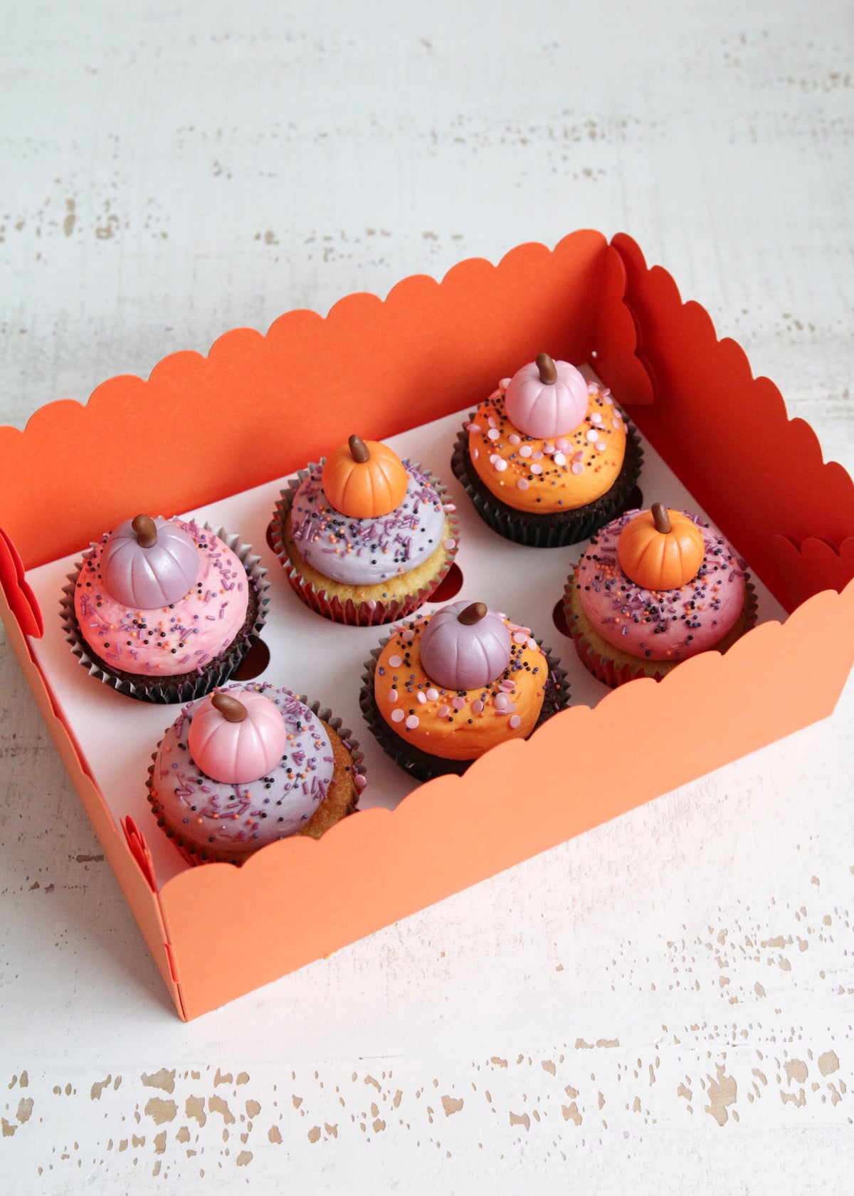 Box of Halloween cupcakes topped with pastel pink, orange and purple buttercream and fondant pumpkins