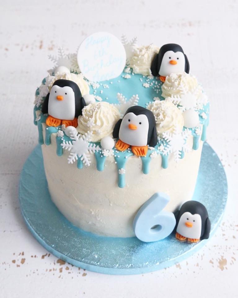 Birthday Cake with Blue Drip, Penguin and Snowflake Decorations and a blue number 6