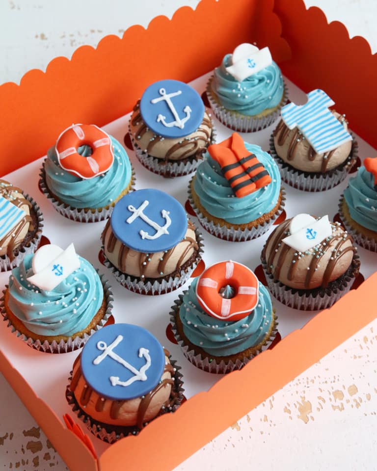 Cupcakes decorated with nautical anchor and sailing themed decorations in a box